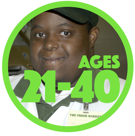 Close up of a smiling young man of color with a developmental disability who is wearing a work uniform with green cap and white polo shirt with green color. Name tag says The Fresh Market.