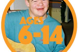 Teenage boy with Down syndrome in blue shirt, smiling, playing guitar.