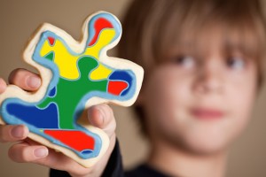 A 9 year old boy holding out a blue iced puzzle piece shaped sugar cookie. Shallow DOF, focus on cookie only.