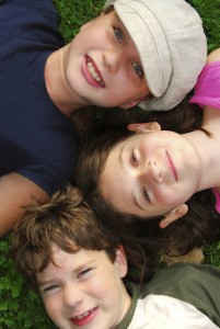 Portrait of three young children lying on grass looking up