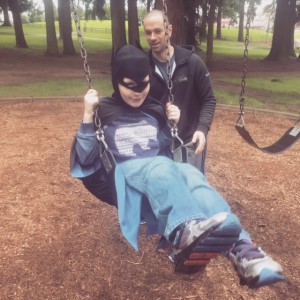 Father pushing son on a swing. Son is dressed as batman.