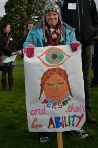 Woman at rally holds sign that reads: See the person and their ability.