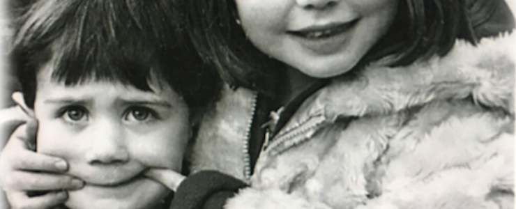 Black and white photo of a brother and sister. Sister is making a face with her hands on her brother's face.