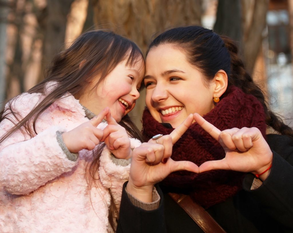 mother and daughter, smiling and making heart shapes with hands.