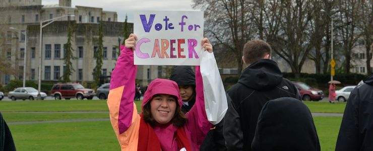 Young adult holding up a sign on the capitol campus in Olympia that reads: Vote for CAREER.
