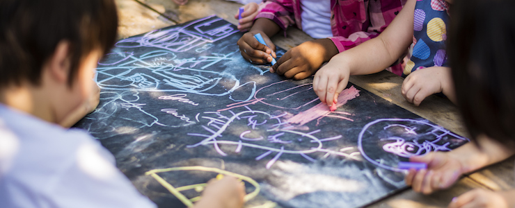 Children drawing art on chalkboard outdoors.