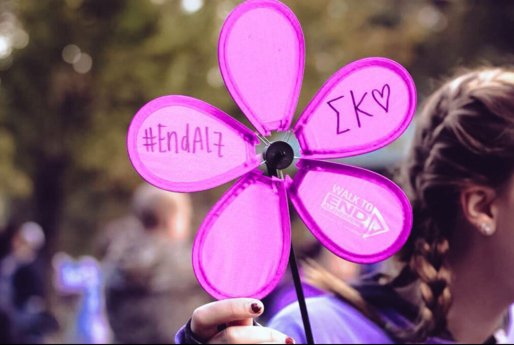 Oudoor gathering (blurred). In forefront, a purple paper flower with #endalz messages on the petals.