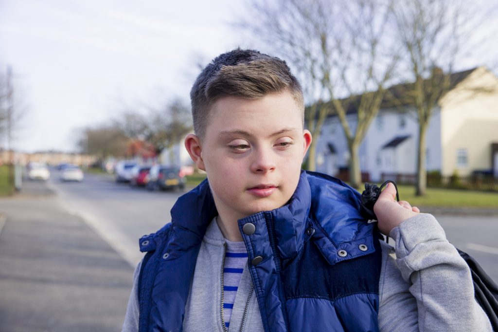 A young man with Down syndrome carries a bag as he walks along a street.