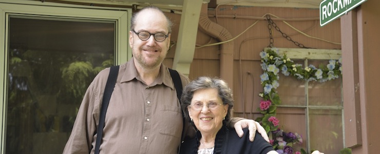 Senior mother and son, standing on porch, smiling.