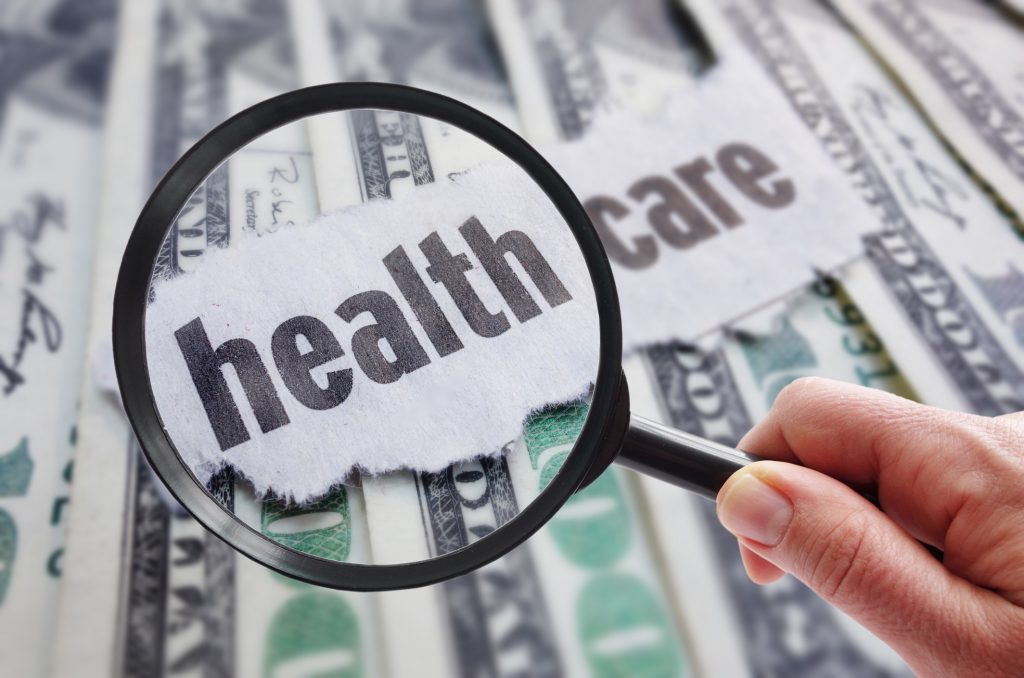 Magnifying glass looking at health care newspaper headline, on cash