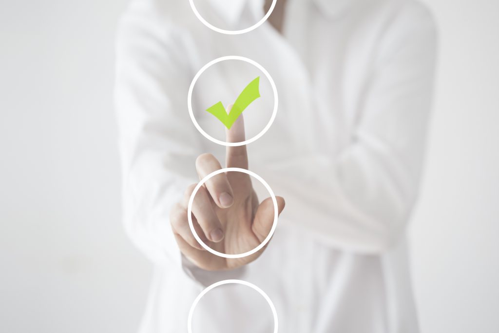 Woman in white, set against white background, touching button in foreground and ticking lime green check box.