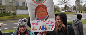 Disability advocates hold a sign that reads See the person and their ability.