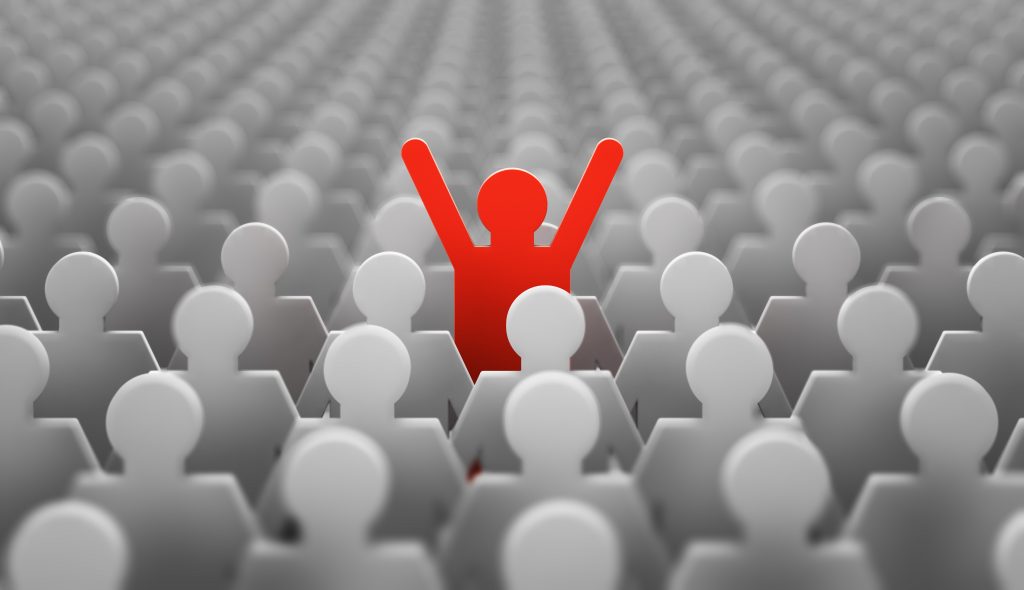 A red paper cut out stick figure raising its arms above a crowd of gray shaded paper cut out people.