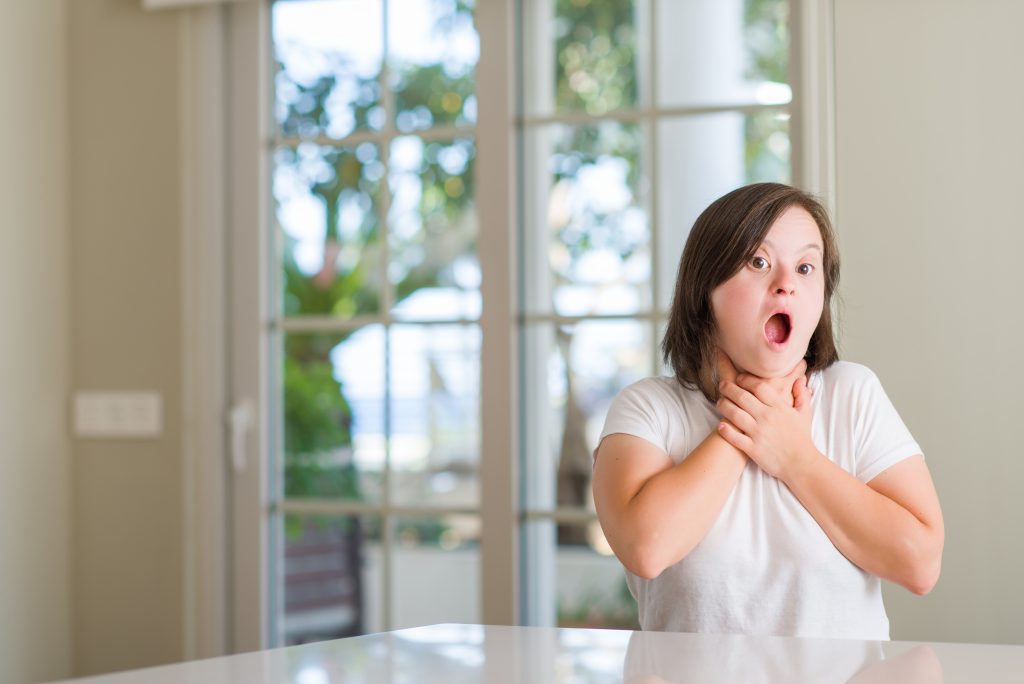 Down syndrome woman at home, holding hands to throat, indicating choking.