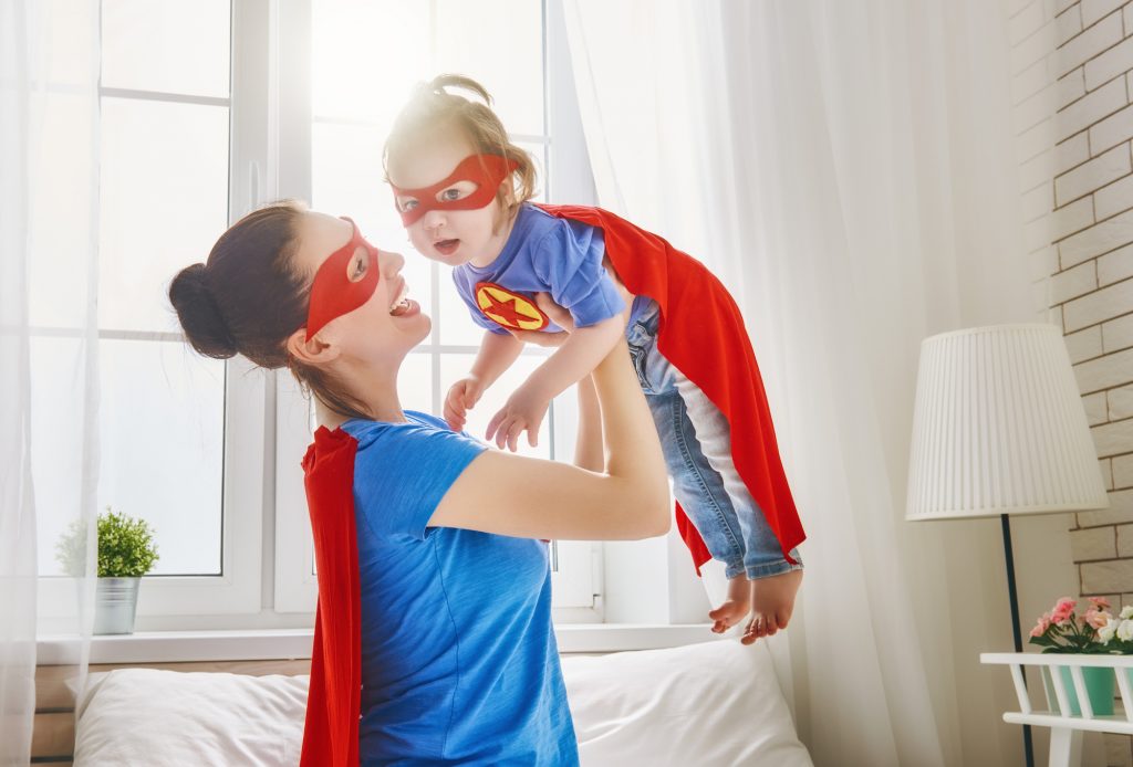 Mother and her child playing together. Girl and mom in Superhero costume. Mum and kid having fun, smiling and hugging. Family holiday and togetherness. (Mother and her child playing together. Girl and mom in Superhero costume. Mum and kid having fun,