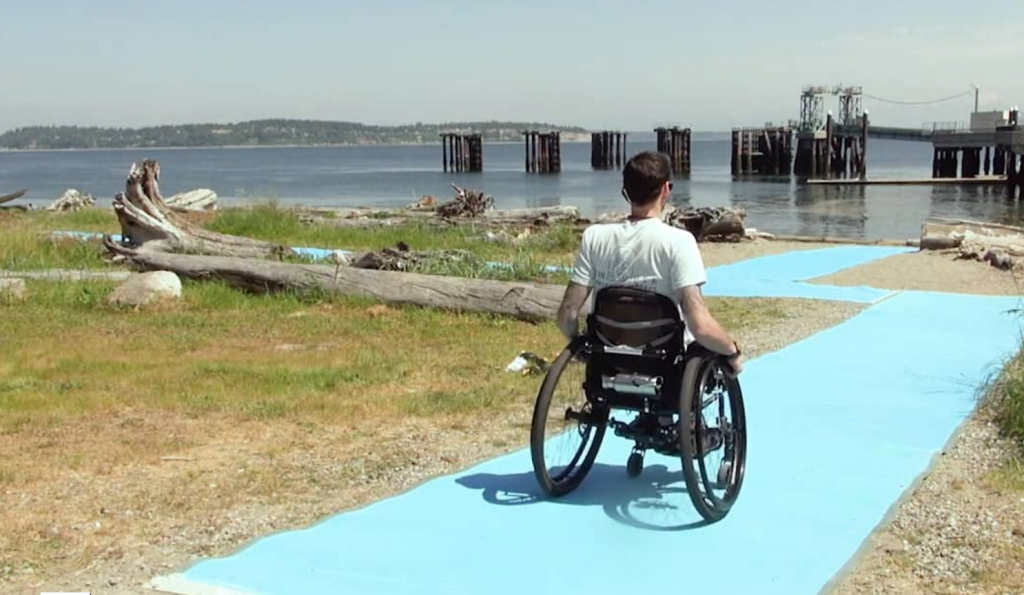 Man in wheelchair on accessbile beach trail next to Puget Sound waters..