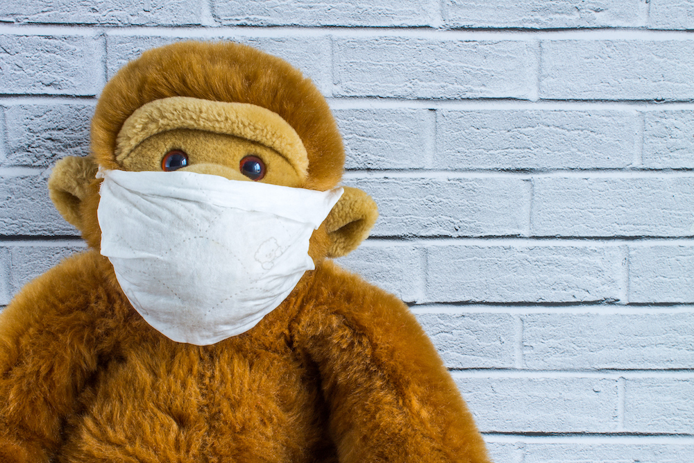 Toy plush monkey in a homemade medical mask on the background of a brick wall with space for copying. Concept - protection from coronavirus.
