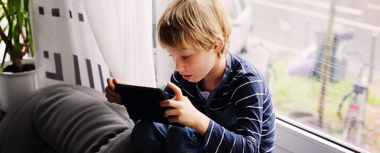 7 year old boy sitting near the window and playing tablet