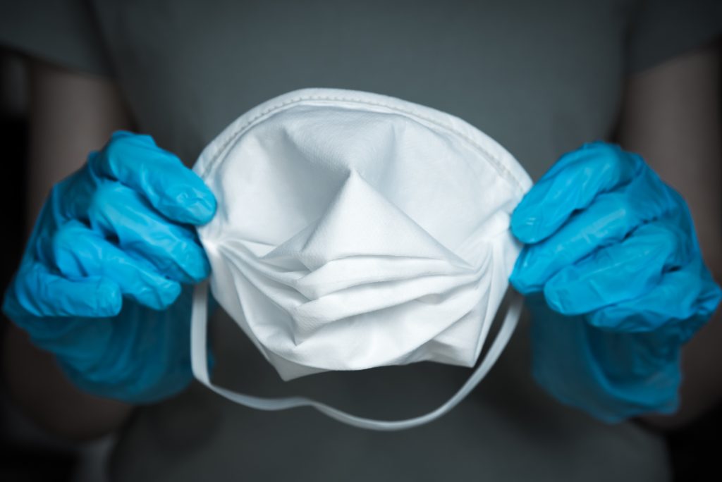 Close-up of hands wearing blue nitrile gloves and holding an N95 medical face mask